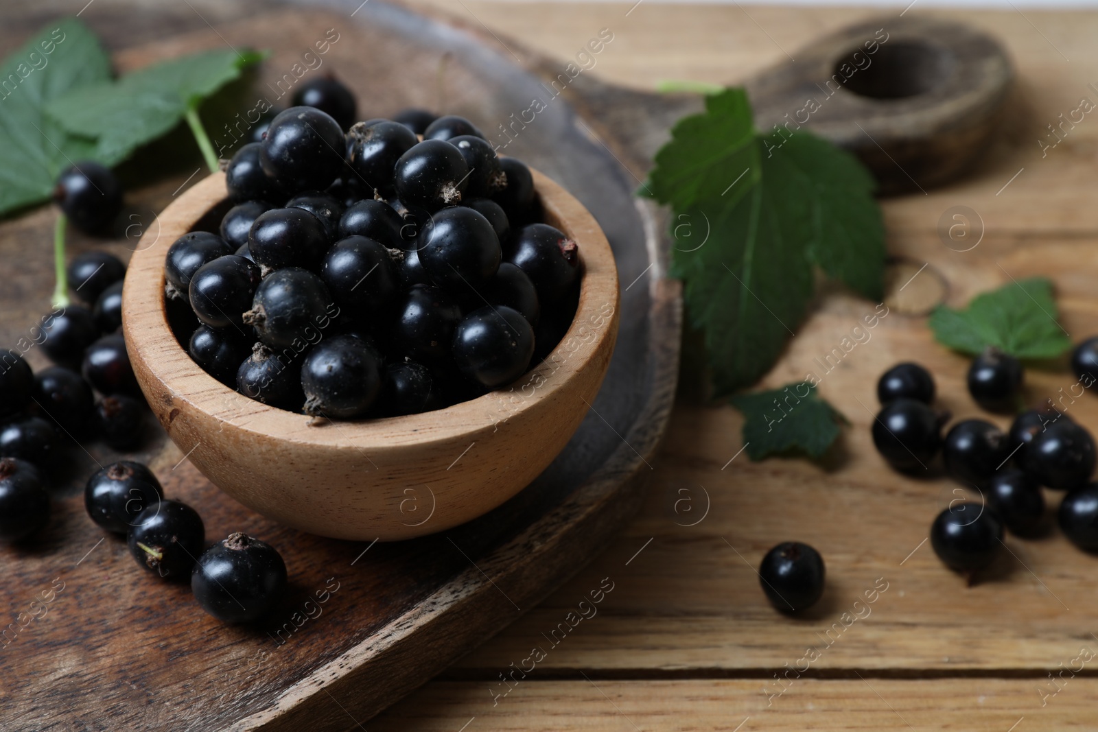 Photo of Ripe blackcurrants and leaves on wooden table, closeup