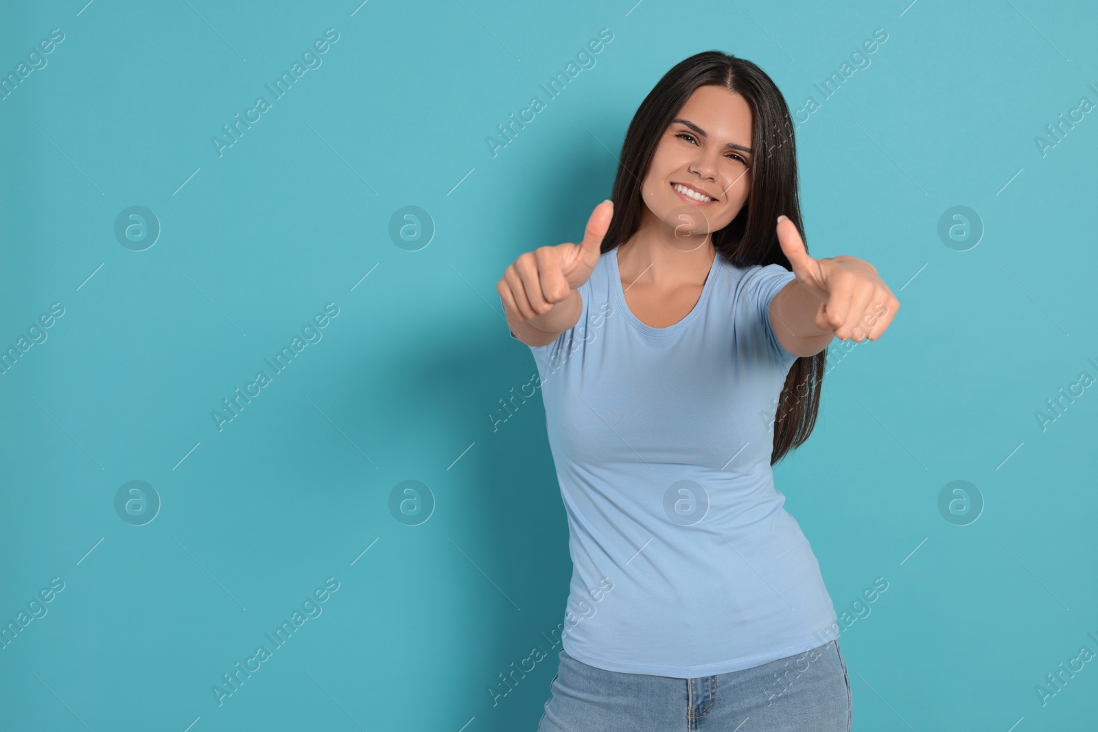 Photo of Young woman showing thumbs up on light blue background, space for text