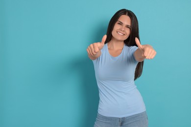 Photo of Young woman showing thumbs up on light blue background, space for text
