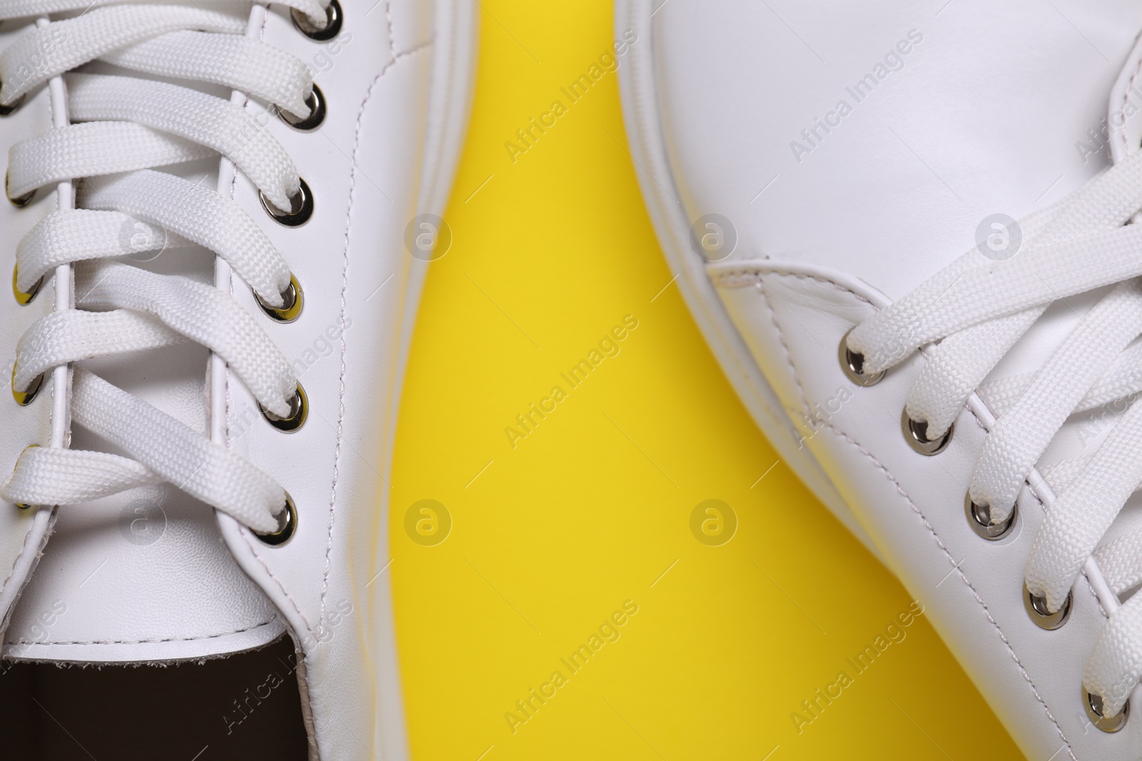 Photo of Pair of stylish white sneakers on yellow background, top view