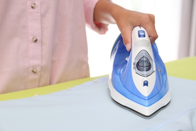 Photo of Young woman ironing clean shirt at home, closeup. Laundry day