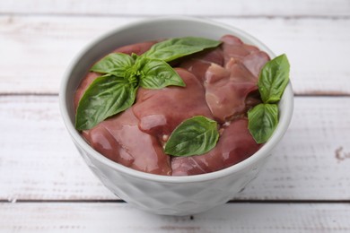 Photo of Bowl with raw chicken liver and basil on white wooden table, closeup