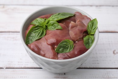 Bowl with raw chicken liver and basil on white wooden table, closeup