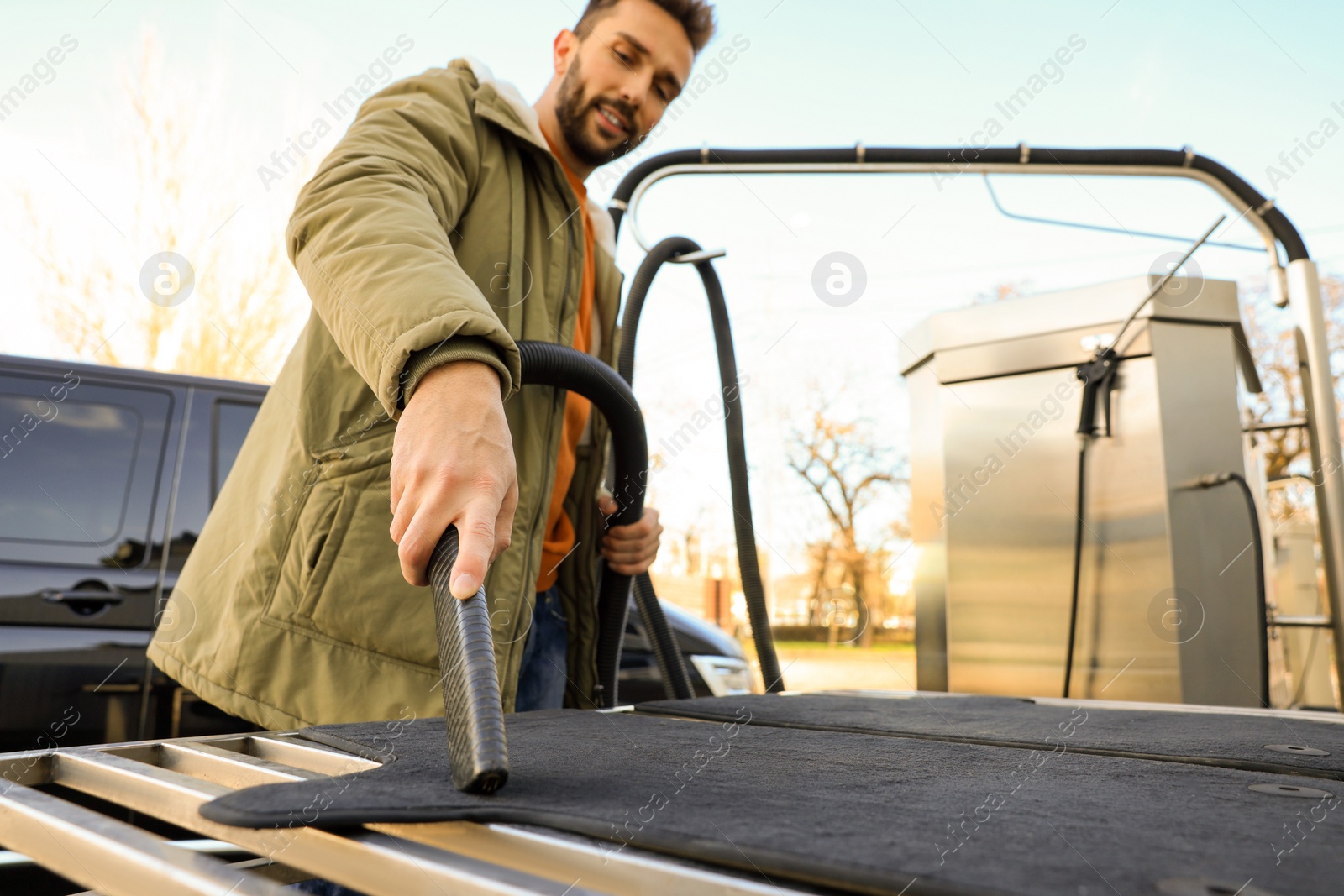 Photo of Man cleaning auto carpets with vacuum cleaner at self-service car wash, low angle view