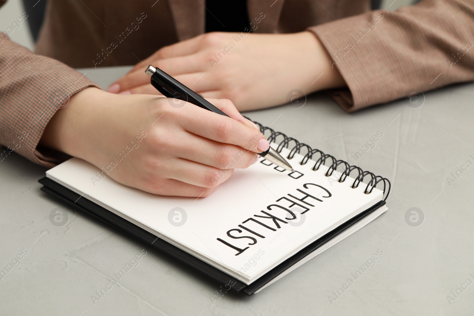Photo of Woman filling Checklist at light grey table, closeup