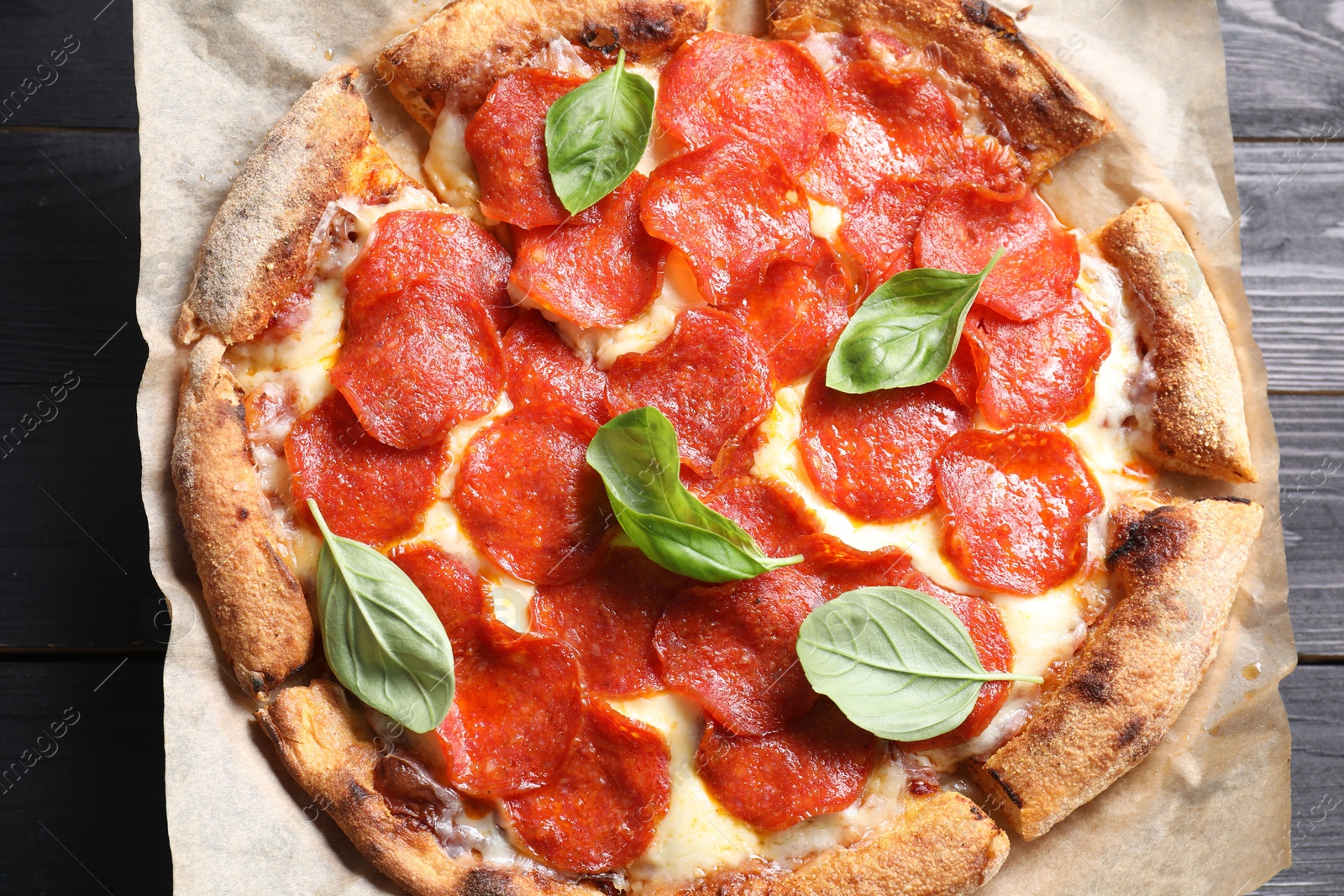 Photo of Tasty pepperoni pizza with basil on black wooden table, top view