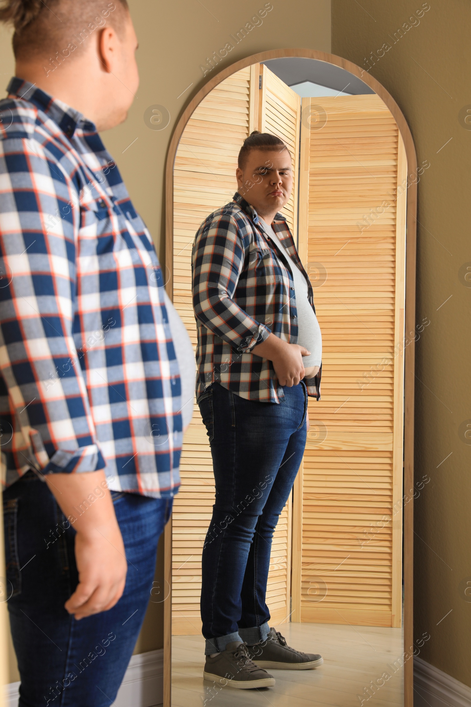 Photo of Overweight man in tight t-shirt near mirror at home