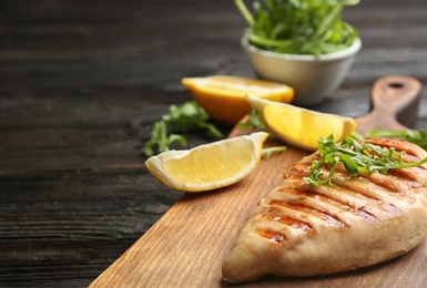 Tasty grilled chicken fillet with lemon and arugula on black table, closeup