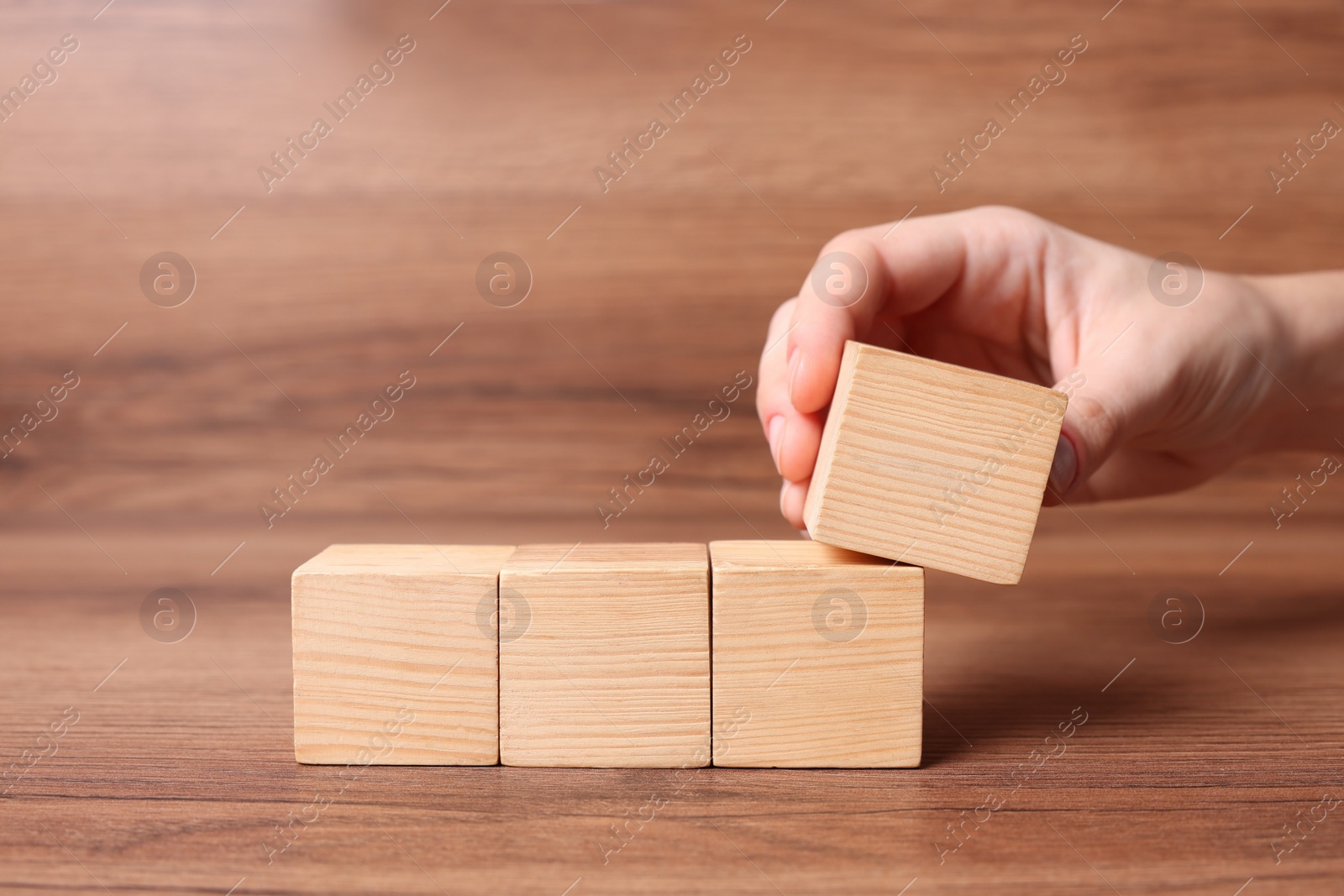 Photo of Woman arranging cubes on wooden background, closeup with space for text. Idea concept