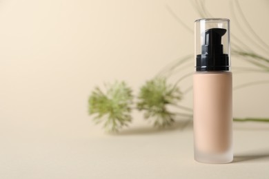 Bottle of skin foundation on beige background, space for text. Makeup product