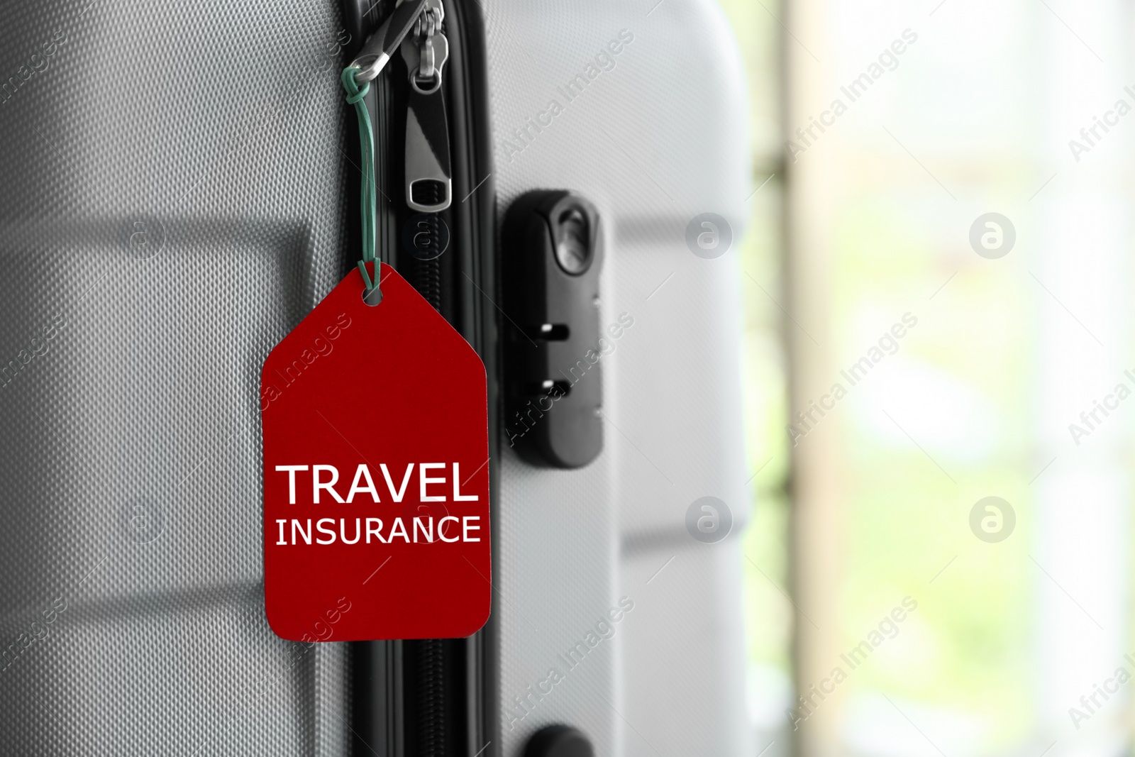 Photo of Stylish suitcase with travel insurance label on blurred background, closeup. Space for text