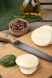 Wooden board with tasty mozzarella slices, basil leaves and knife on table