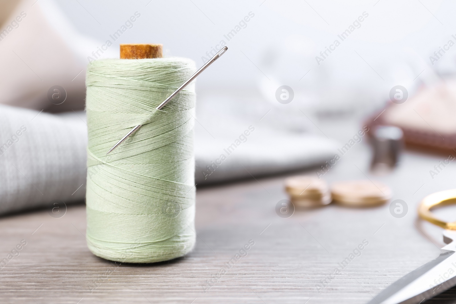 Photo of Spool of light green sewing thread with needle and scissors on wooden table, space for text