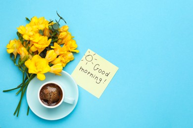 Photo of Cup of aromatic coffee, beautiful yellow freesias and Good Morning note on light blue background, flat lay. Space for text