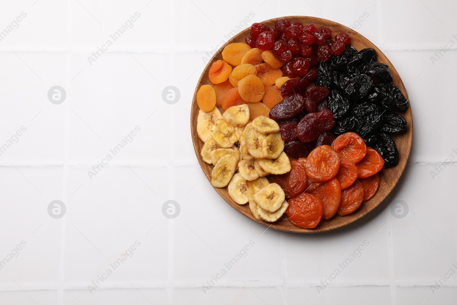 Photo of Delicious dried fruits on white tiled table, top view. Space for text