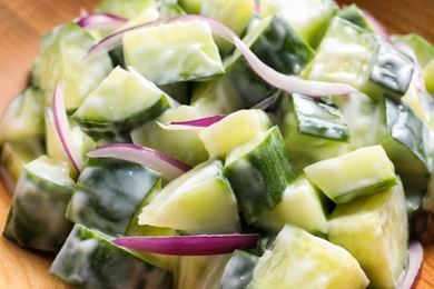 Photo of Fresh creamy cucumber salad in wooden dish, closeup