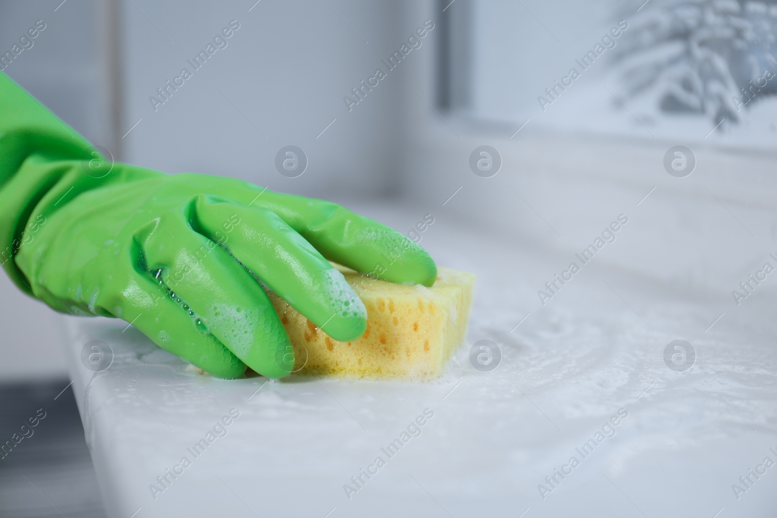 Photo of Woman cleaning window sill with sponge indoors, closeup