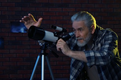 Senior man looking at stars through telescope in room