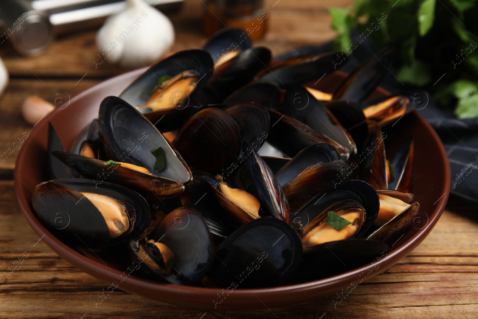 Photo of Plate of cooked mussels with parsley on wooden table, closeup