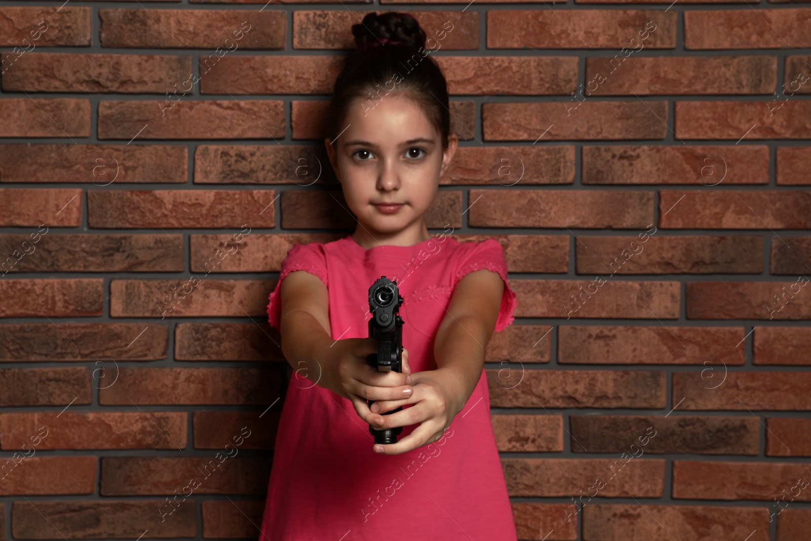 Photo of Little child playing with gun against brick wall. Dangerous game