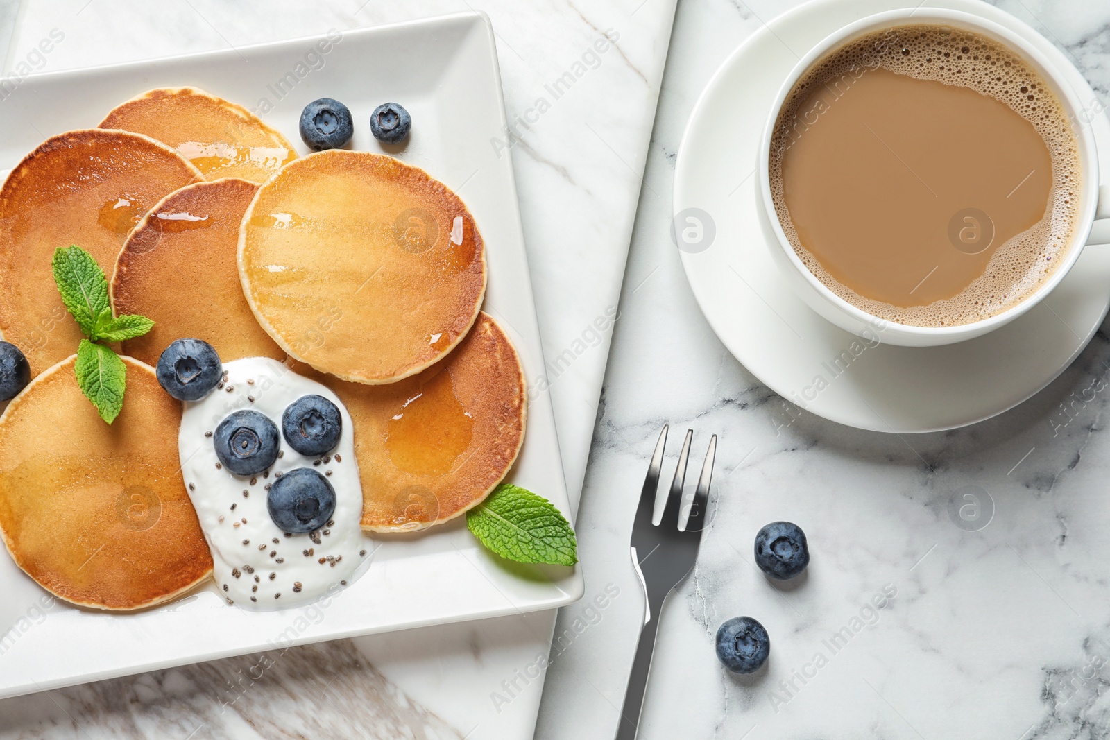 Photo of Plate of tasty pancakes with blueberries, sauce and mint on white marble table, flat lay