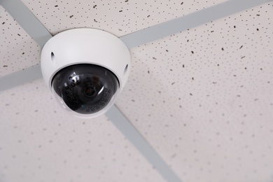 Photo of Modern security CCTV camera on ceiling in office, space for text. Protection system