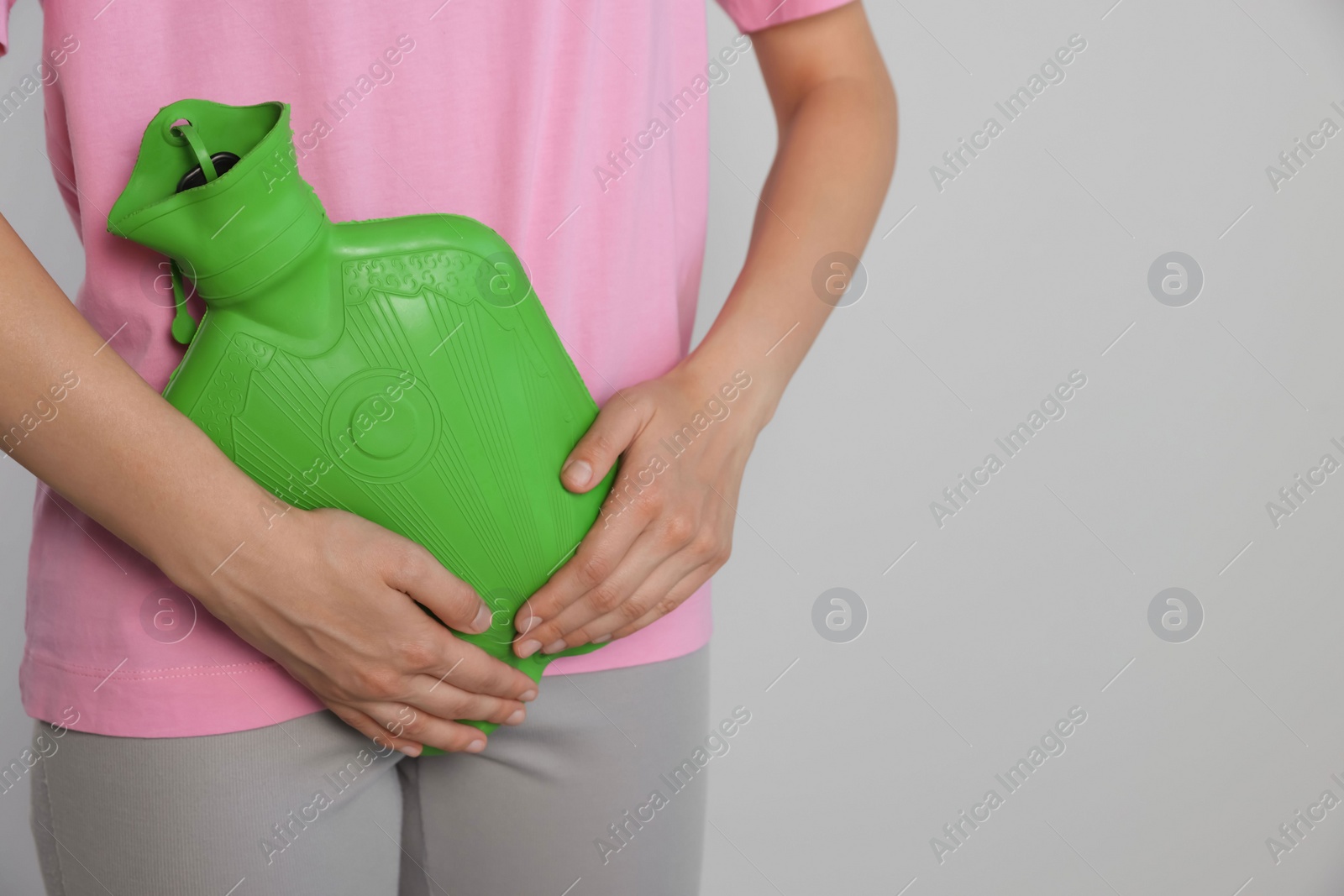 Photo of Woman using hot water bottle to relieve cystitis pain on light background, closeup. Space for text