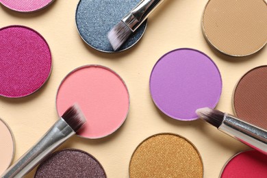 Different beautiful eye shadows and makeup brushes on beige background, flat lay