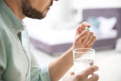 Photo of Young man with pill and glass of water indoors