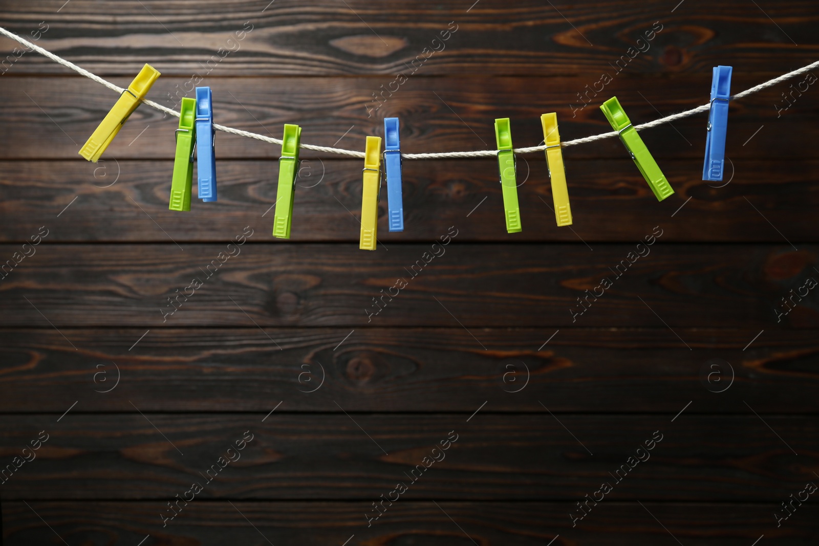 Photo of Colorful plastic clothespins on rope against wooden background. Space for text