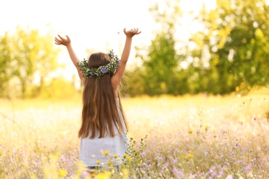 Cute little girl wearing flower wreath outdoors, back view. Child spending time in nature