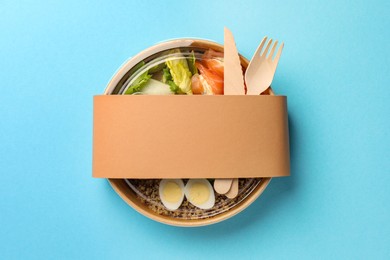 Photo of Tasty food in container with fork and knife on light blue background, top view. Space for text