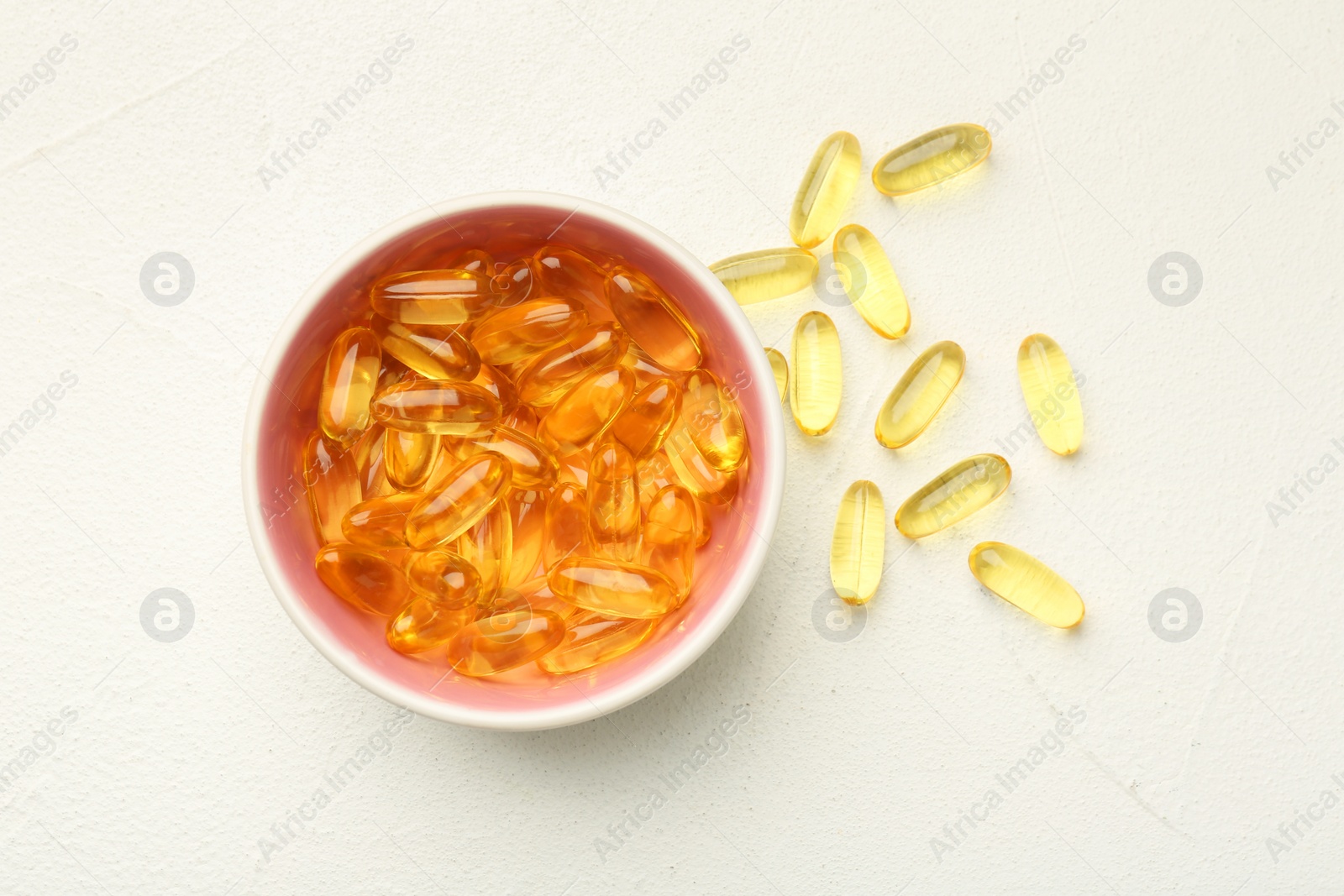 Photo of Vitamin capsules in bowl on white wooden table, top view
