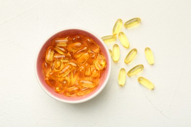 Vitamin capsules in bowl on white wooden table, top view