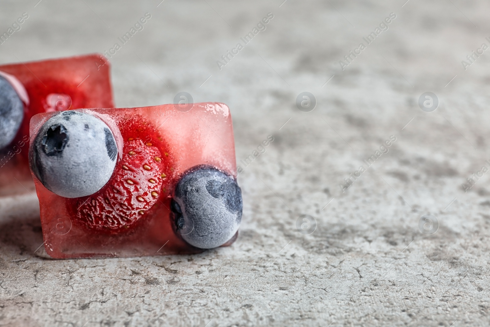 Photo of Ice cubes with berries on table, closeup. Space for text