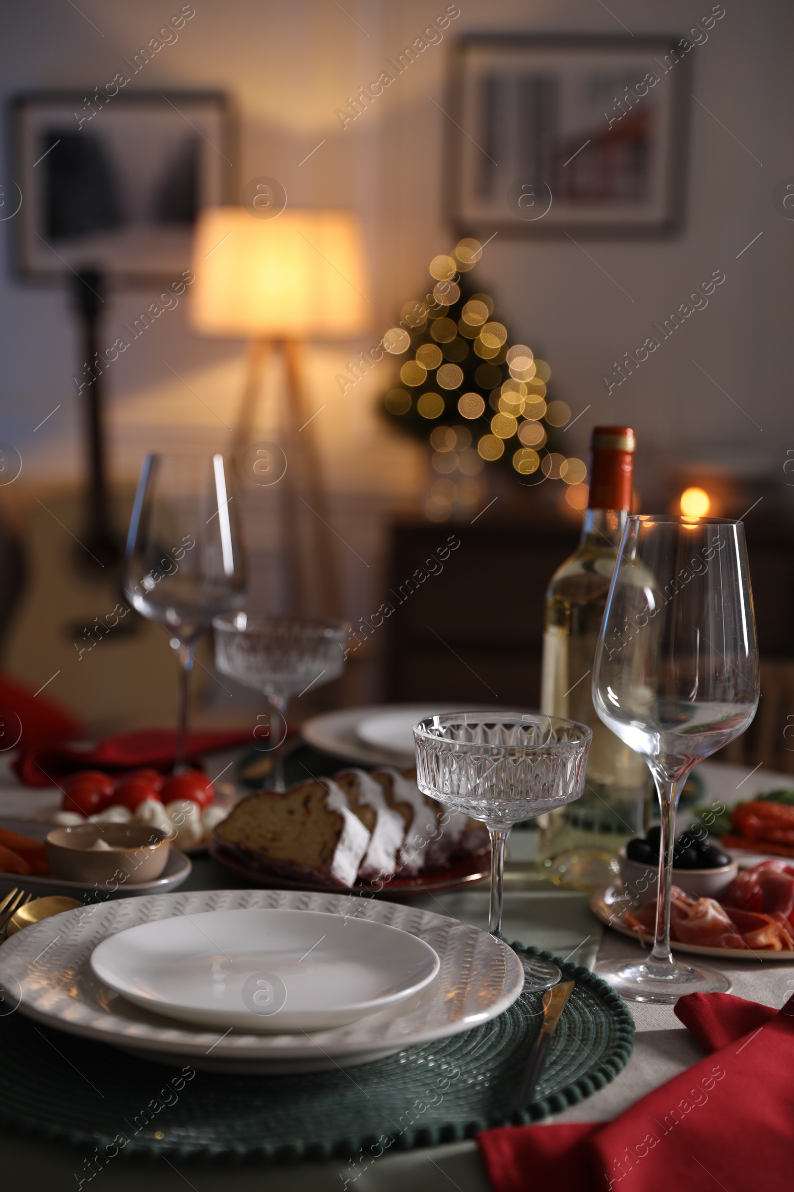 Photo of Christmas table setting with bottle of wine, appetizers and dishware indoors