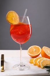 Glass of tasty Aperol spritz cocktail with orange slices on white table against gray background