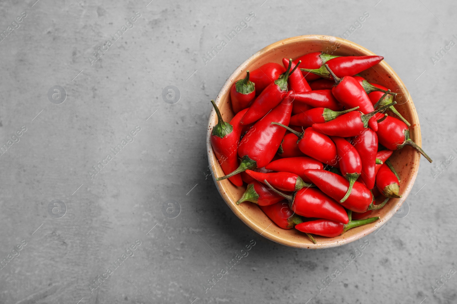 Photo of Red chili peppers in bowl and space for text on gray background, top view