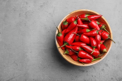 Photo of Red chili peppers in bowl and space for text on gray background, top view