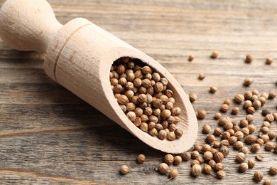 Photo of Scoop with dried coriander seeds on wooden table, closeup