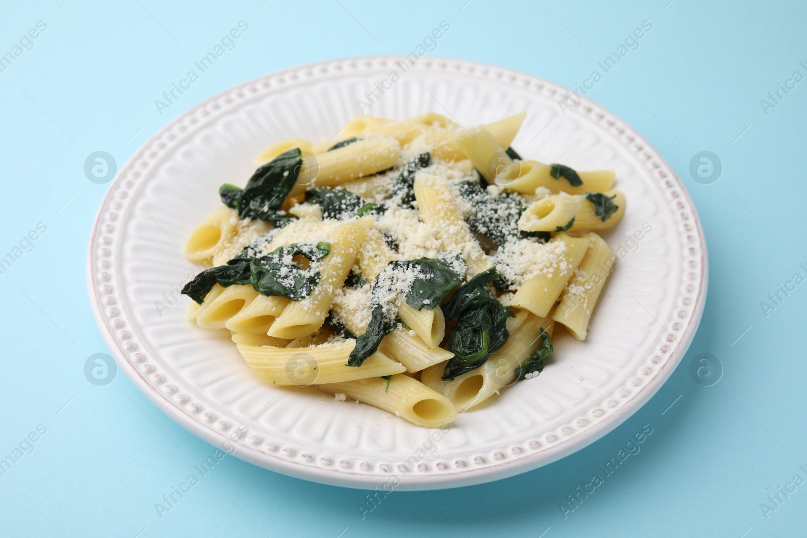 Photo of Tasty pasta with spinach and cheese on light blue table