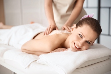 Beautiful young woman having massage with body scrub in spa salon