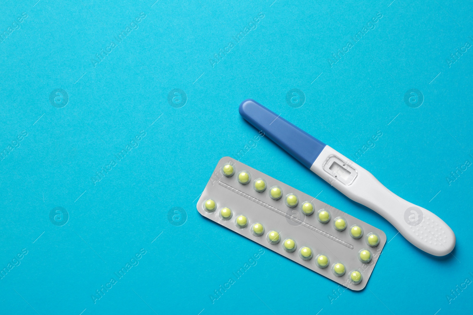 Photo of Birth control pills and pregnancy test on light blue background, top view. Space for text