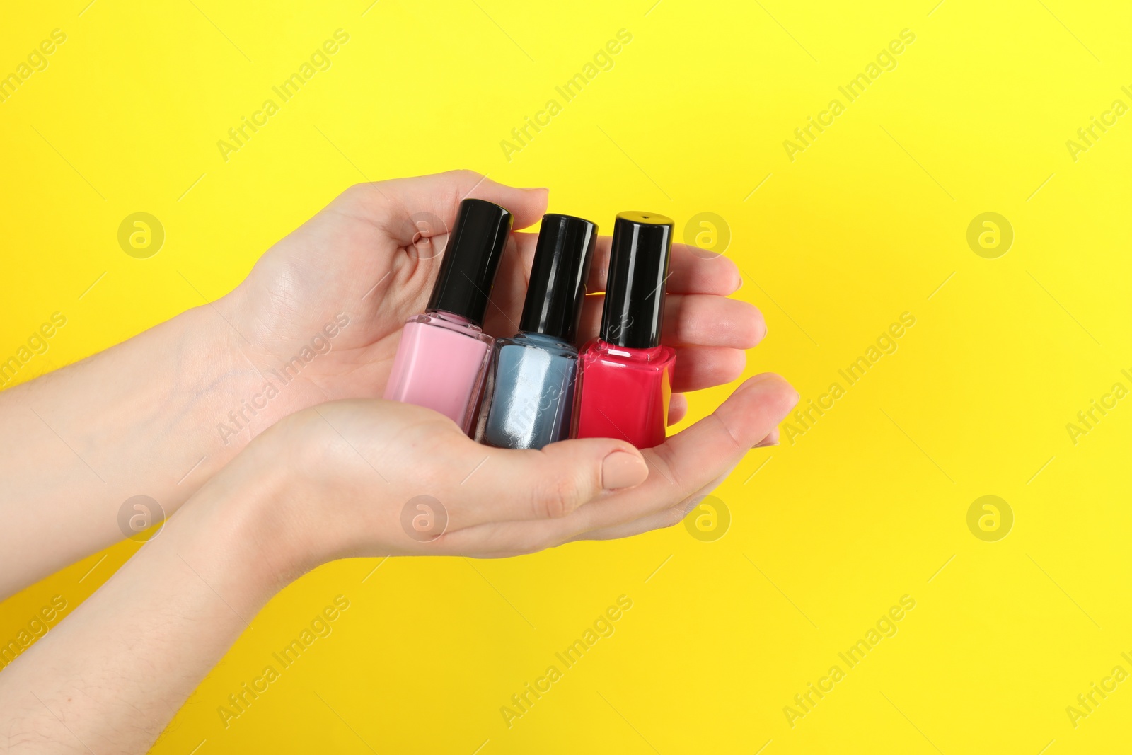 Photo of Woman holding nail polishes on yellow background, closeup