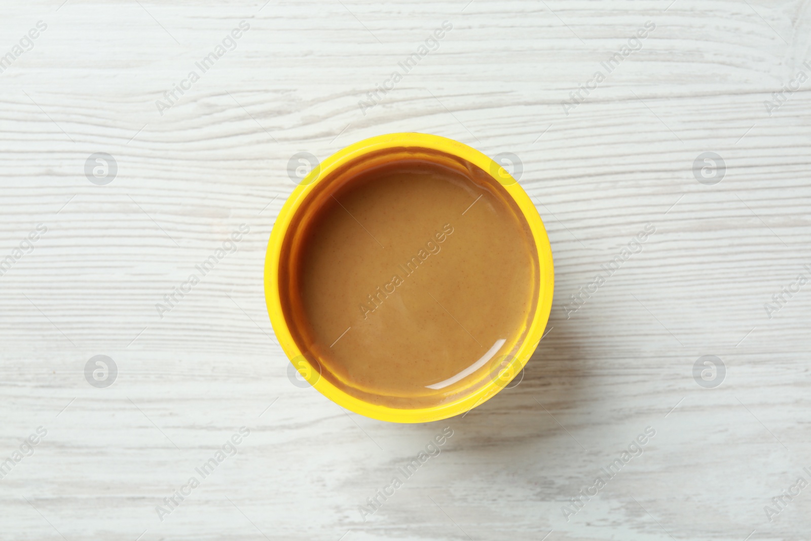 Photo of Spicy mustard in plastic container on white wooden table, top view