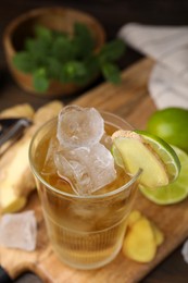 Photo of Glass of tasty ginger ale with ice cubes and ingredients on wooden table, closeup