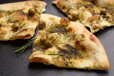 Photo of Delicious focaccia bread with green olives on slate board, closeup