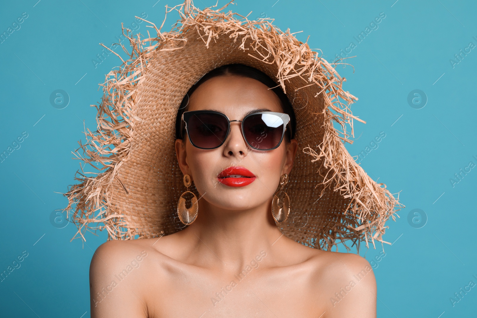 Photo of Attractive woman in fashionable sunglasses and wicker hat against light blue background