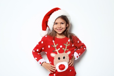 Photo of Cute little girl in Christmas sweater and hat on white background