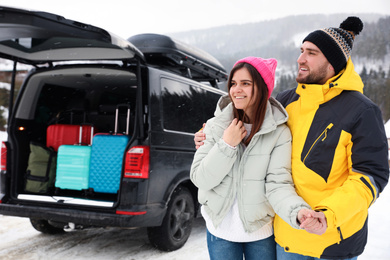 Happy couple near car with open trunk on snowy road. Winter vacation